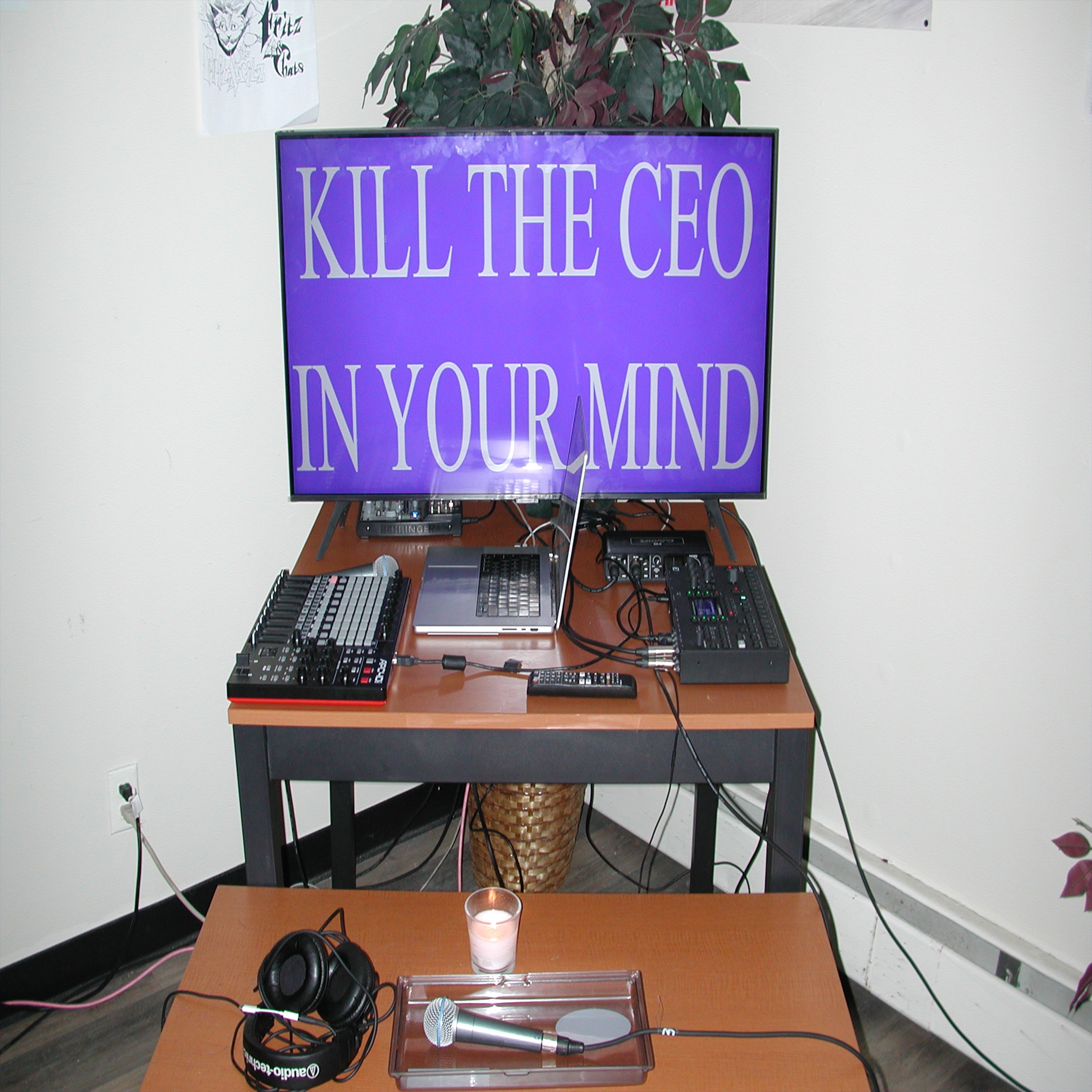 An image of the stage setup at one of the band's first shows, a television sits in the back and says 'Kill the CEO in your mind' a bottle of Hennessy is in the foreground